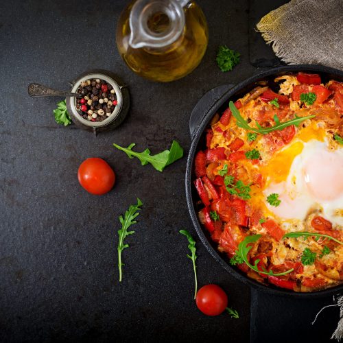 Breakfast. Fried eggs with vegetables - shakshuka in a frying pan on a black background in the Turkish style. Flat lay. Top view